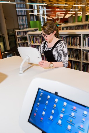 Delwedd merch yn defnyddion ipad mewn llyfrgell